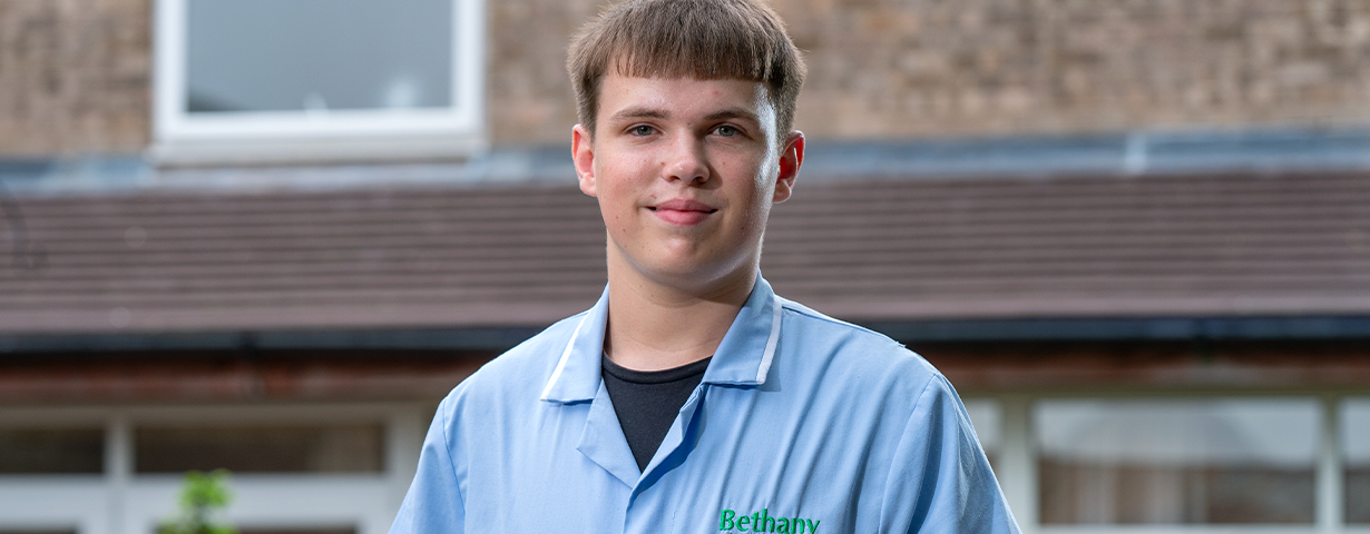 Male Health & Social Care Apprentice stood outside his place of work in a blue uniform